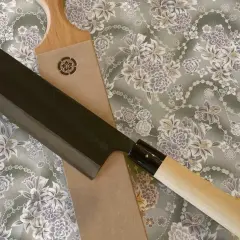 En vacker strigla kniv med mörkt blad och ljust trähandtag ligger på ett tyg med blomstermönster.
