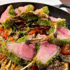 Saftigt lamm med perfekt lamm temperatur, täckt av gröna örter, serveras med grillade grönsaker i en gjutjärnspanna.
