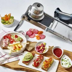En mandolin förbereder grönsaker för en festlig måltid. Skivade rödbetor och morötter ligger bredvid smörgåsar med avokado och tomat.