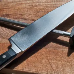 En kockslipar kniv mot ett skärpstål på en träskärbräda.