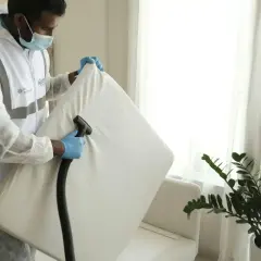 Professionell rengöring för att få bort kisslukt från soffa. En person i skyddsdräkt använder en dammsugare på en soffdyna.