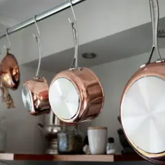 Kopparkastruller hänger på en stång. En vitlöksfläta hänger bredvid. Här är några kopparputs tips för att hålla dem skinande.