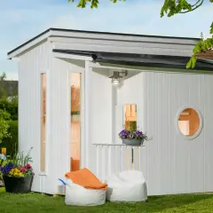 En vit lekstuga liten med fönster och en rund öppning. Uteplats med sittpuffar och blommor.