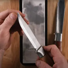 Händer som håller en kniv mot en bryna. En annan kniv ligger bredvid.