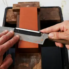 Händer slipar en kniv mot en orange sten. En skärpa som gör matlagningen enklare.