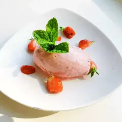 En portion krämig jordgubbsglass, gjord med en frozen yoghurt glassmaskin, dekorerad med färska jordgubbar och mynta.