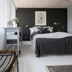 Ett modernt svart sovrum med en stor säng, konst på väggen och en grå byrå.