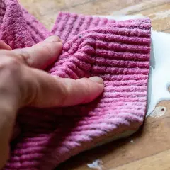 En hand håller en rosa trasa för att torka upp en vit vätska på en träyta.