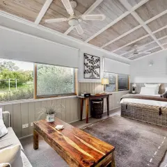 Mysig sovrum med lantlig inredning inspiration. Säng med korgförvaring, soffa med sjöhästkudde och träbord. Stora fönster med utsikt över grönskan.