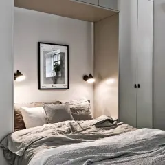 Ett inrett litet sovrum med en inbjudande säng, två vägglampor och konst på väggen.