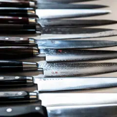 En rad vassa kockknivar, redo för ett kockkniv test. Vackra handtag i trä och metall, med blanka blad.