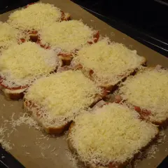 Flera smörgåsar med ost, tomat och skinka ligger på en plåt, redo för **toast i ugn**.