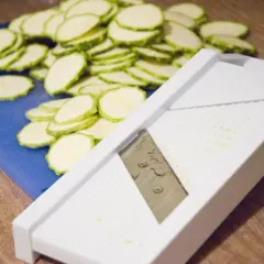 En hög med skivade squash ligger bredvid en bra mandolin.