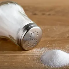 En saltkvarn ligger på ett träbord med en liten hög salt bredvid.