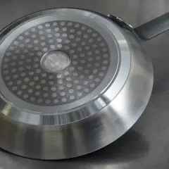 En stekpanna med induktionsbotten ligger på en metallbänk. Ska man diska stekpannan med diskmedel?