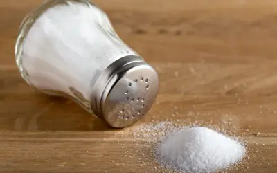 En saltkvarn ligger på ett träbord med en liten hög salt bredvid.