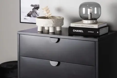 Svart byrå med två lådor, dekorerad med en kruka med torkad växt och böcker. Perfekt byrå sovrum inspiration.