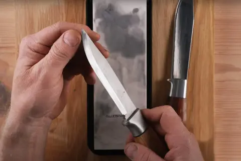 Händer som håller en kniv mot en bryna. En annan kniv ligger bredvid.