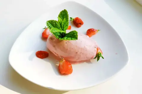 En portion krämig jordgubbsglass, gjord med en frozen yoghurt glassmaskin, dekorerad med färska jordgubbar och mynta.