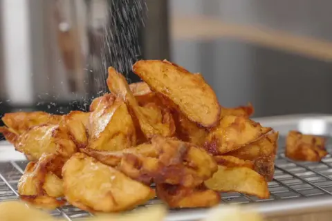 Krispiga pommes frites, perfekt frityr temp, strös salt över en hög gyllene potatisklyftor på ett galler.