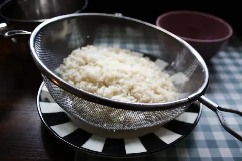 Nykokt ris rinner av i ett durkslag. Snart dags att koka mer ris i kastrull.