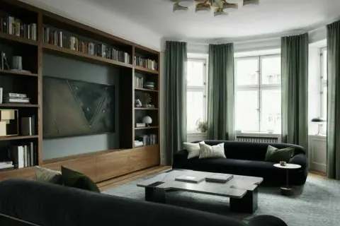 En elegant bokhylla med inbyggd TV och konst ger bokhylla inspiration till ett modernt vardagsrum med mörk soffa och gröna gardiner.