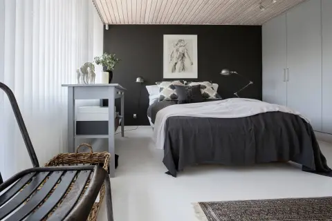 Ett modernt svart sovrum med en stor säng, konst på väggen och en grå byrå.