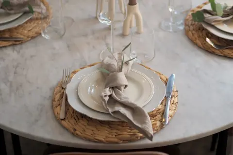 En modern juldukning med linneservetter, vita tallrikar och glas på en marmorbord.