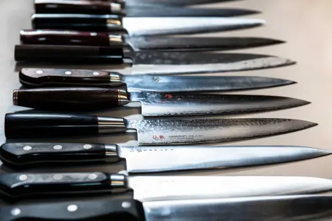 En rad vassa kockknivar, redo för ett kockkniv test. Vackra handtag i trä och metall, med blanka blad.