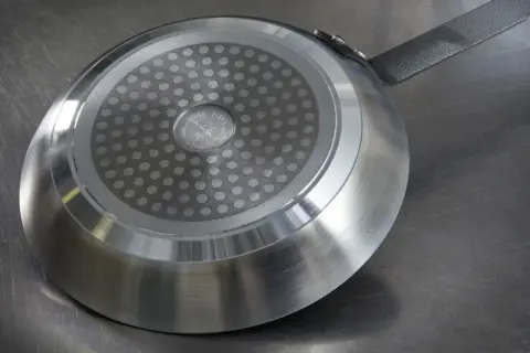 En stekpanna med induktionsbotten ligger på en metallbänk. Ska man diska stekpannan med diskmedel?