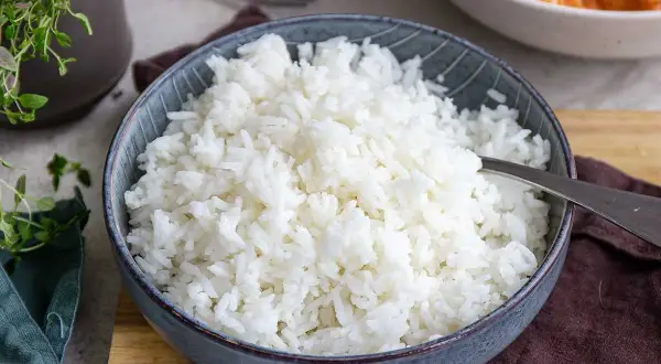 En skål med fluffigt basmatiris, perfekt för att koka med rätt mått. Bredvid syns en annan skål med en krämig gryta.