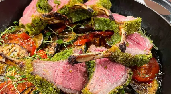 Saftigt lamm med perfekt lamm temperatur, täckt av gröna örter, serveras med grillade grönsaker i en gjutjärnspanna.