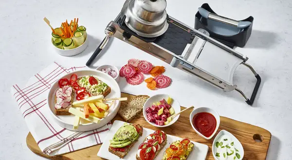 En mandolin förbereder grönsaker för en festlig måltid. Skivade rödbetor och morötter ligger bredvid smörgåsar med avokado och tomat.
