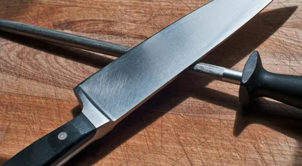 En kockslipar kniv mot ett skärpstål på en träskärbräda.