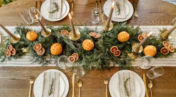 Juldukning inspiration med granris, apelsiner med nejlikor, torkade apelsinskivor och ljus. En vacker och doftande bordsdekoration.