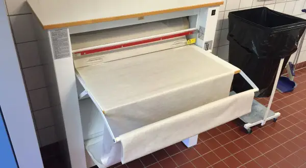 Stor mangel med ett vitt lakan som rullas ut. En stor svart soptunna står bredvid.