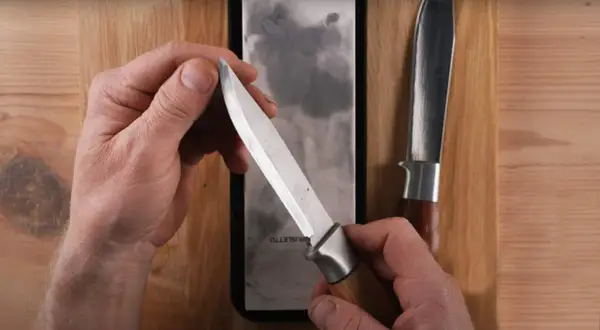 Händer som håller en kniv mot en bryna. En annan kniv ligger bredvid.
