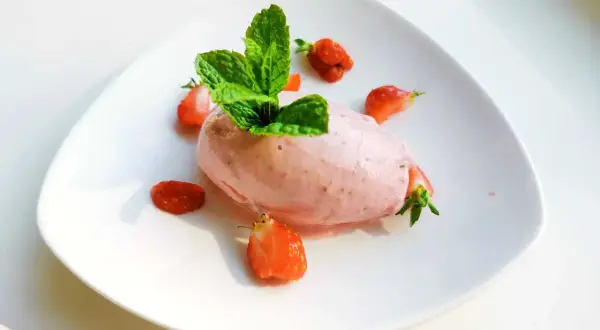 En portion krämig jordgubbsglass, gjord med en frozen yoghurt glassmaskin, dekorerad med färska jordgubbar och mynta.