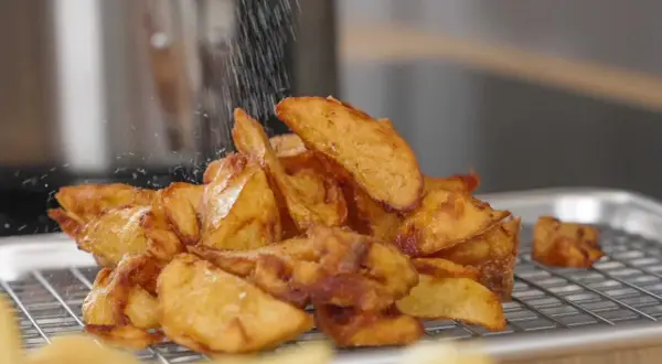 Krispiga pommes frites, perfekt frityr temp, strös salt över en hög gyllene potatisklyftor på ett galler.
