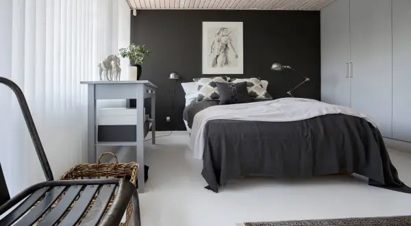 Ett modernt svart sovrum med en stor säng, konst på väggen och en grå byrå.