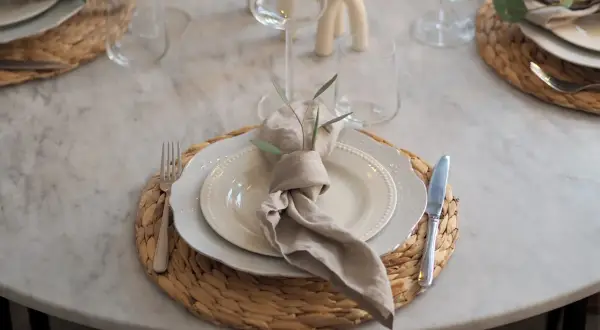 En modern juldukning med linneservetter, vita tallrikar och glas på en marmorbord.