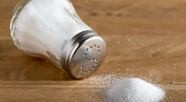 En saltkvarn ligger på ett träbord med en liten hög salt bredvid.