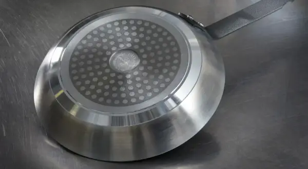 En stekpanna med induktionsbotten ligger på en metallbänk. Ska man diska stekpannan med diskmedel?