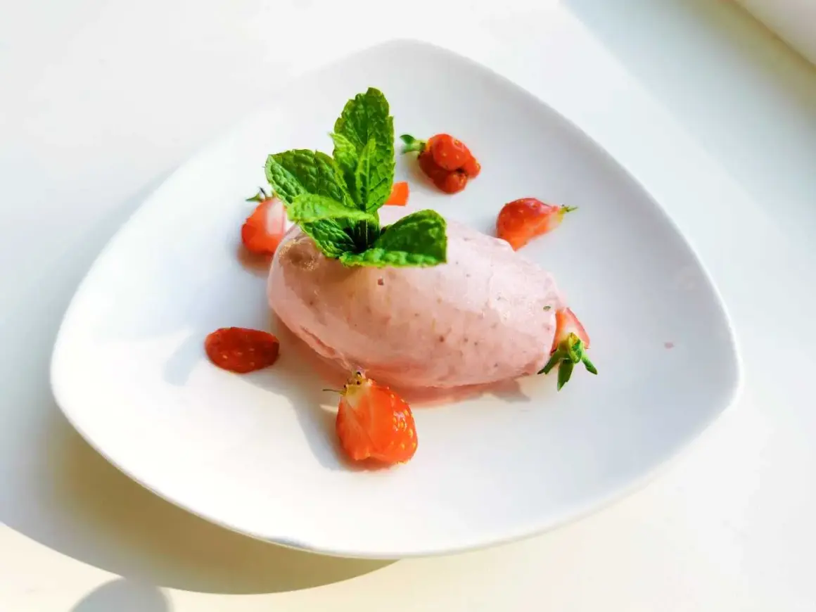En portion krämig jordgubbsglass, gjord med en frozen yoghurt glassmaskin, dekorerad med färska jordgubbar och mynta.