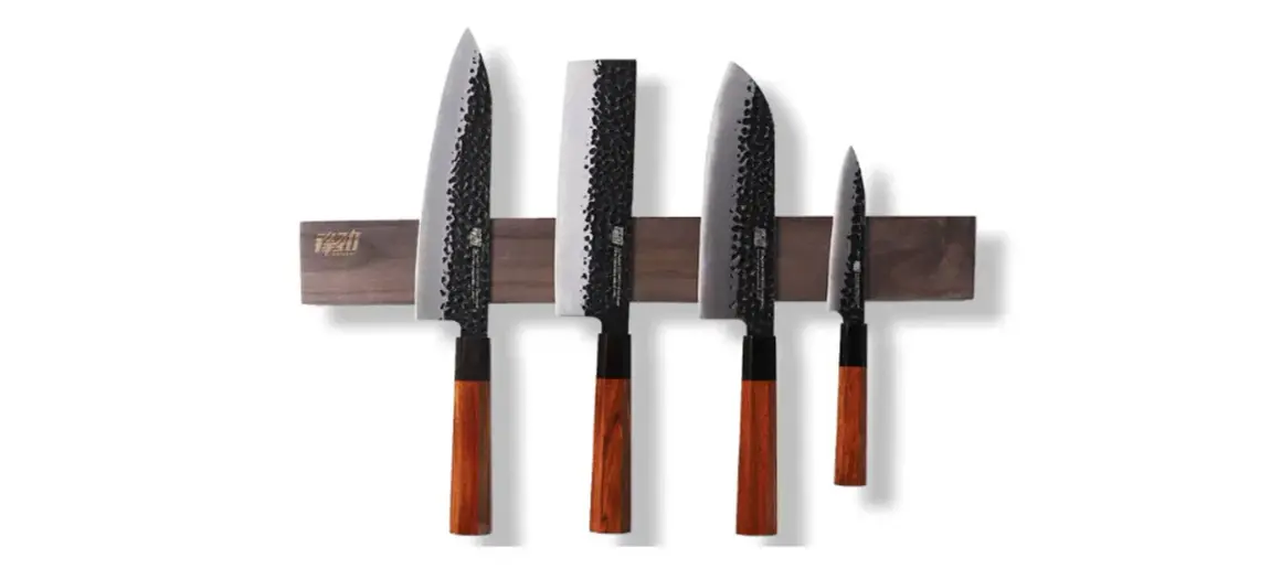 Fyra japanska knivar med hamrad yta och trähandtag, monterade på en magnetisk trälist. En samling som representerar den bästa japanska kniven för ditt kök.