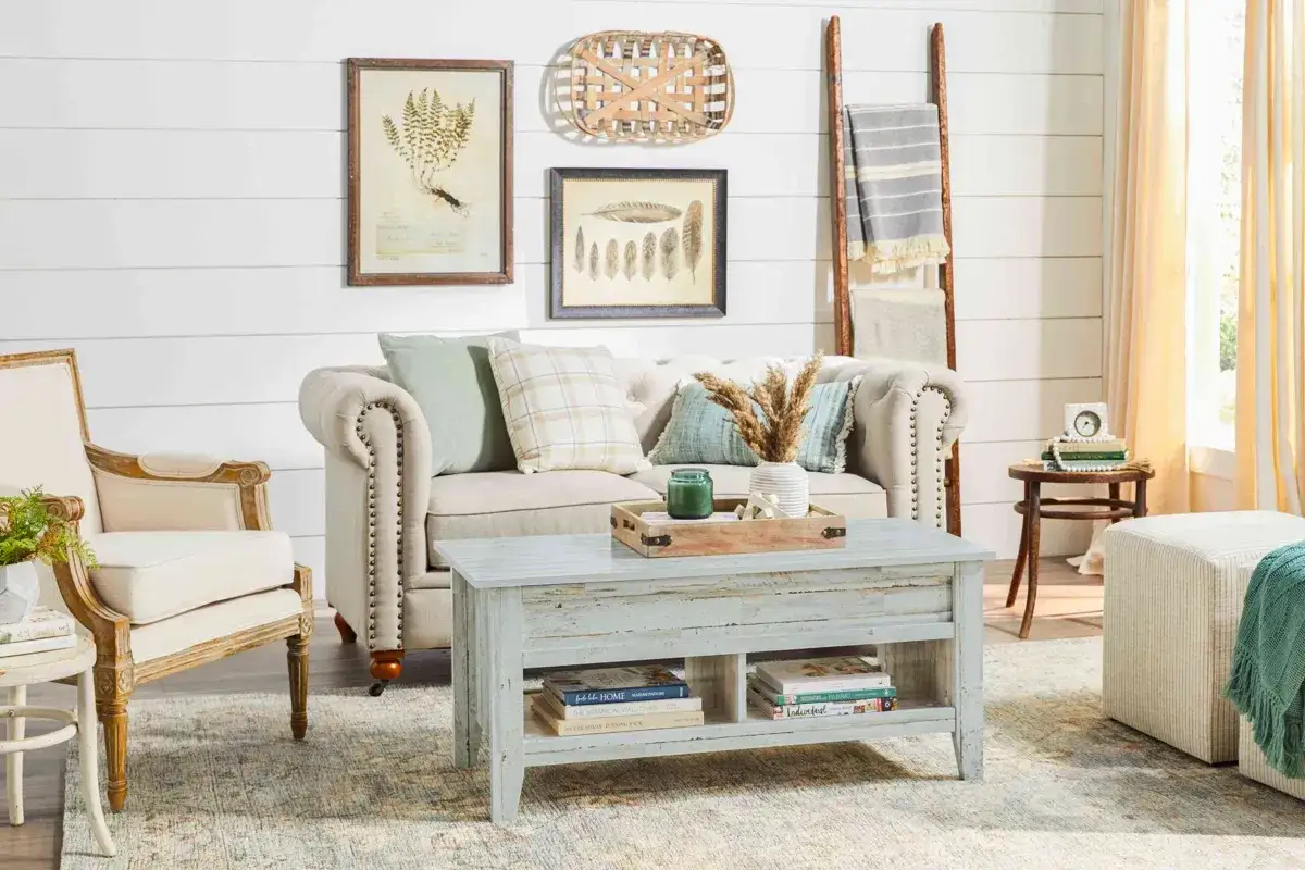 En soffa och f&aring;t&ouml;lj i shabby chic inredning. Ett soffbord med f&ouml;rvaring, kuddar och en vas med torkade blommor.
