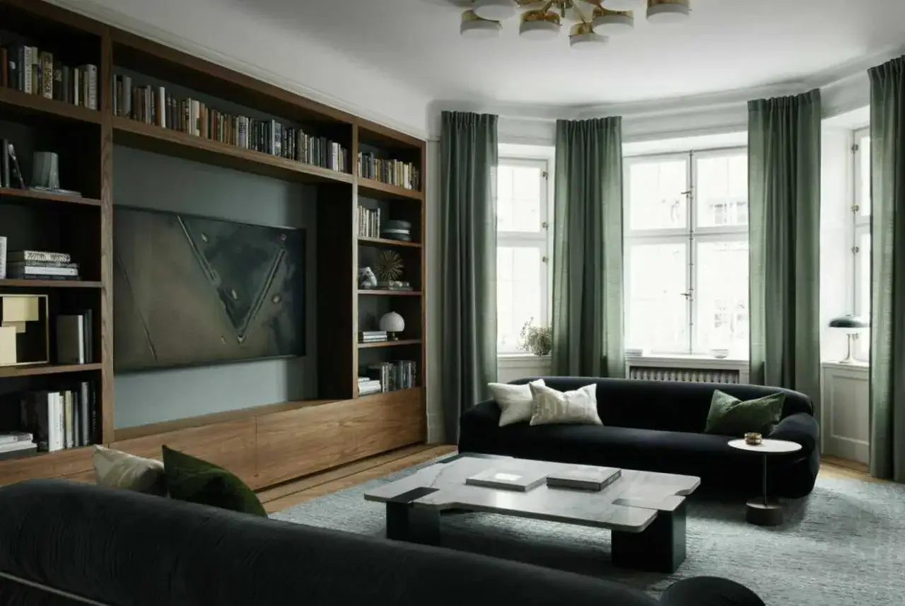 En elegant bokhylla med inbyggd TV och konst ger bokhylla inspiration till ett modernt vardagsrum med m&ouml;rk soffa och gr&ouml;na gardiner.