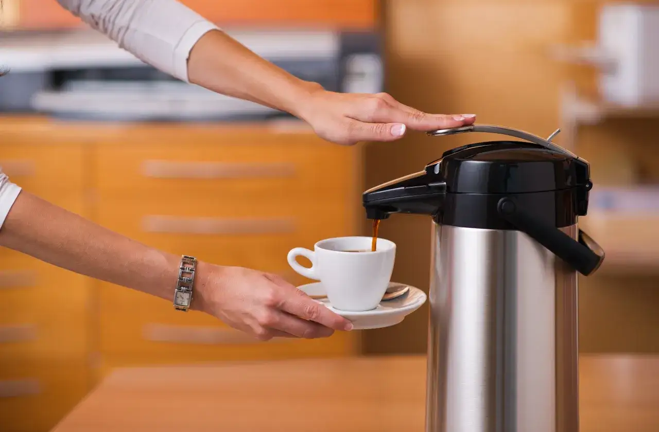 En hand häller upp kaffe från en termos i en kopp. Termosen är redo för diskmaskinen efter användning.