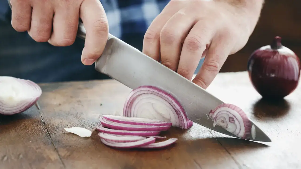 Händer skär rödlök i tunna skivor med en kockkniv. Ett perfekt kockkniv test för att se hur lätt det är att skiva grönsaker.
