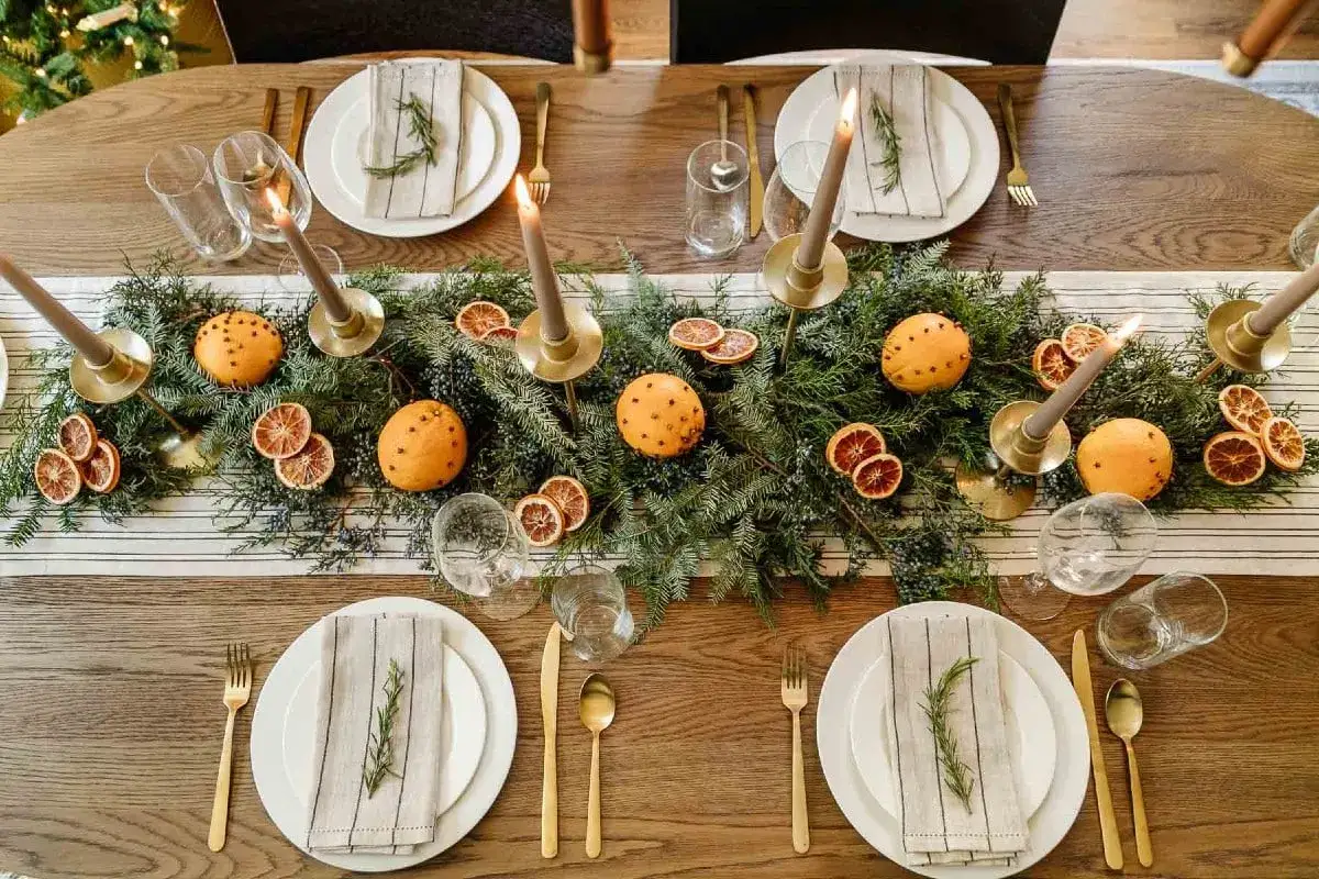 Juldukning inspiration med granris, apelsiner med nejlikor, torkade apelsinskivor och ljus. En vacker och doftande bordsdekoration.